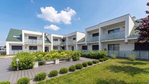 A modern multi-story building with balconies, a landscaped garden, and a clear sky. - Cozy Studio with a Balcony | Parking (Grzybowo)