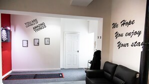 Een gang met motiverende kunst aan de muur, een deur, een zwarte leren bank en een dartbord.
