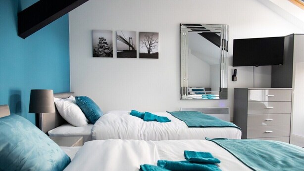Een moderne hotelkamer met twee bedden, een flatscreen televisie, een spiegel en kunst aan de muur.