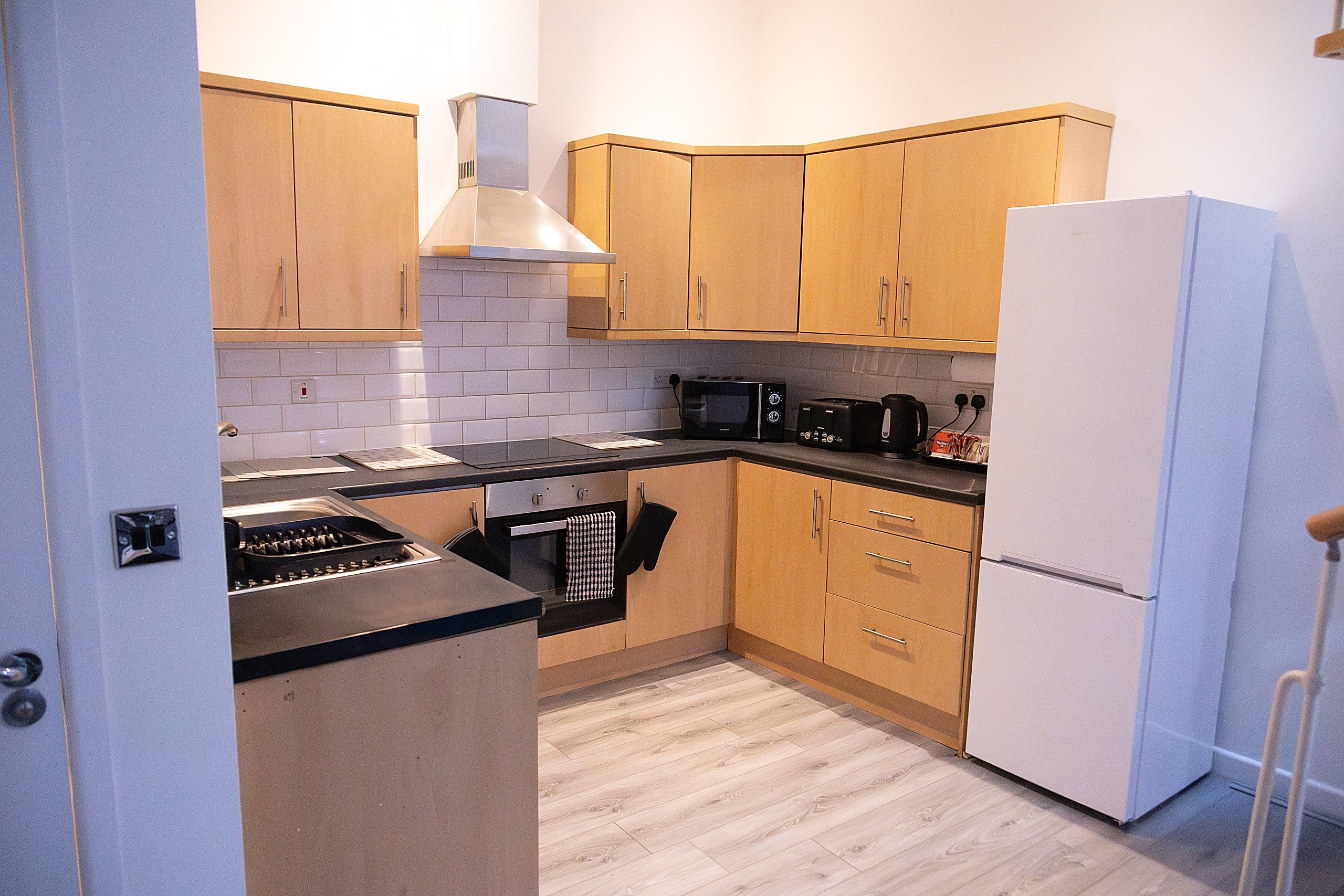 A compact kitchen with wooden cabinets, a microwave, a toaster, and a refrigerator.