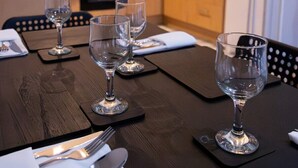 Een eettafel gedekt met wijnglazen, bestek en servetten in een moderne keuken met houten kastjes en een rvs afzuigkap.