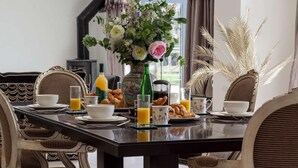 Une table à manger dressée avec des aliments pour le petit-déjeuner, un vase de fleurs et une vue sur l’extérieur.
