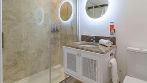 Une salle de bain moderne dotée d’une douche à parois de verre, d’un lavabo en marbre et d’un miroir rond avec éclairage intégré.