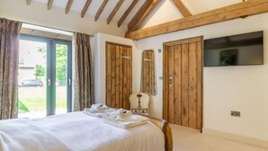 A bedroom with a bed, wooden wardrobe, a mirror, and a TV on the wall. - 3 Bed in Lowestoft (oc-82802) (Lound)