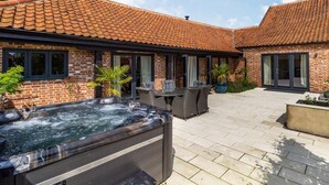 A brick building with a tiled roof, a hot tub, outdoor seating, and potted plants. - 3 Bed in Lowestoft (oc-82802) (Lound)