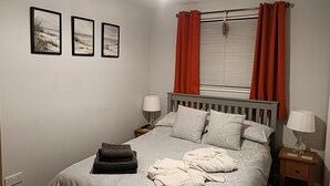 Una camera da letto con un letto, due comodini, una finestra con tende e tre quadri appesi al muro.