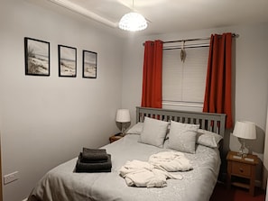 A bedroom with a bed, two bedside tables, a window with curtains, and three framed pictures on the wall. - 1 Bed in Cinderford (oc-82884) (Cinderford)