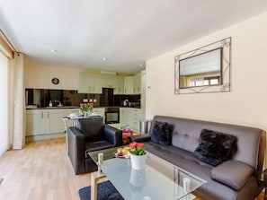 A modern living room with a sofa, a glass coffee table, and a kitchen in the background. - 1 Bed in Cinderford (oc-82884) (Cinderford)