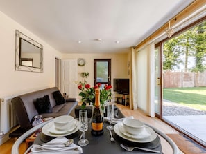 A dining area with a table set for four, a sofa, a television, and a view of the outdoors. - 1 Bed in Cinderford (oc-82884) (Cinderford)