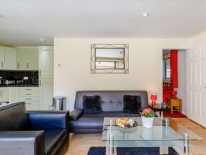 A modern living room with a sofa, a glass coffee table, and a dining area with a red table lamp. - 1 Bed in Cinderford (oc-82884) (Cinderford)