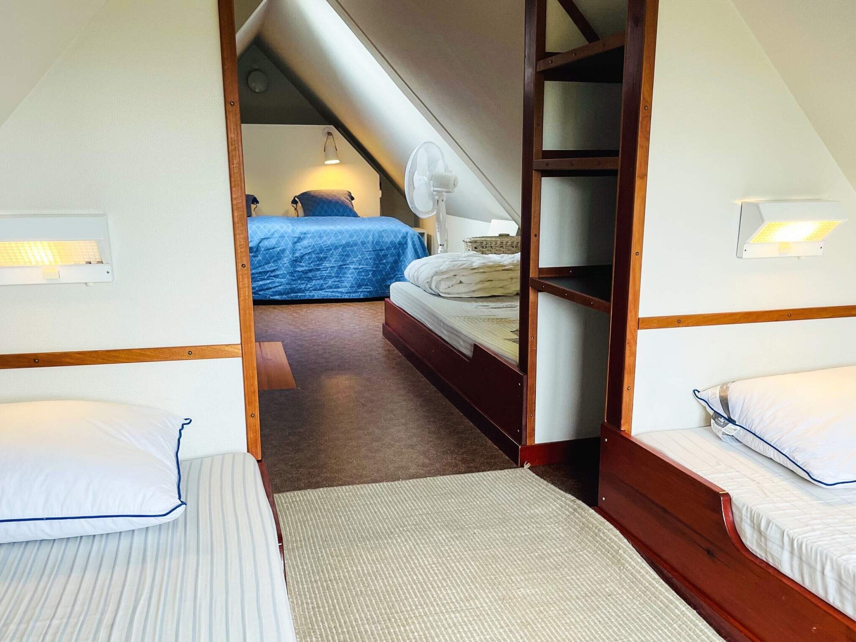 A room with two beds, a wooden wardrobe, a ceiling fan, and a small window.
