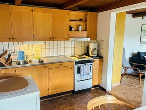 A kitchen with wooden cabinets, a stove, a sink, and a coffee maker. - 5 Person Holiday Home in Kivik (Kivik)