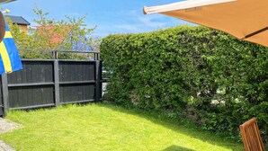Ein gepflegter Garten mit Holzzaun, einer Hecke und einer Terrasse mit einem Stuhl.