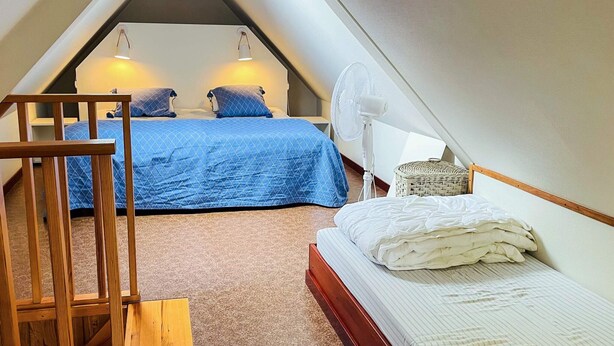 Ein kleines, dreieckiges Schlafzimmer im Dachgeschoss mit zwei Betten, einem Standventilator und einer Holztreppe.