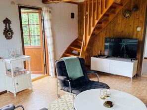 A room with a wooden staircase, a television on a white cabinet, a black chair with a green throw, and a white table with glasses. - 5 Person Holiday Home in Kivik (Kivik)