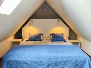 A bedroom with a sloped ceiling, two bedside lamps, a bed with a blue quilt, and a pillow with a blue pattern. - 5 Person Holiday Home in Kivik (Kivik)