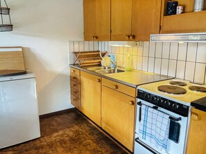 A compact kitchen with wooden cabinets, a white refrigerator, a stove with a kettle, and a sink. - 5 Person Holiday Home in Kivik (Kivik)