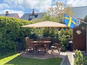 A patio with a table and chairs, a flag, and a hedge. - 5 Person Holiday Home in Kivik (Kivik)