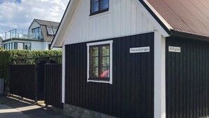 Ein kleines, einstöckiges Gebäude mit dunkler Fassade und weißem Zierrat. Auf dem Gebäude befinden sich zwei Schilder, eines mit der Aufschrift 'Hommebodvågen' und das andere mit 'Mellbygrand'.
