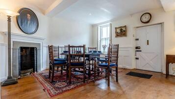 A dining room with a fireplace, wooden chairs, a table set for four, and a large painting on the wall.