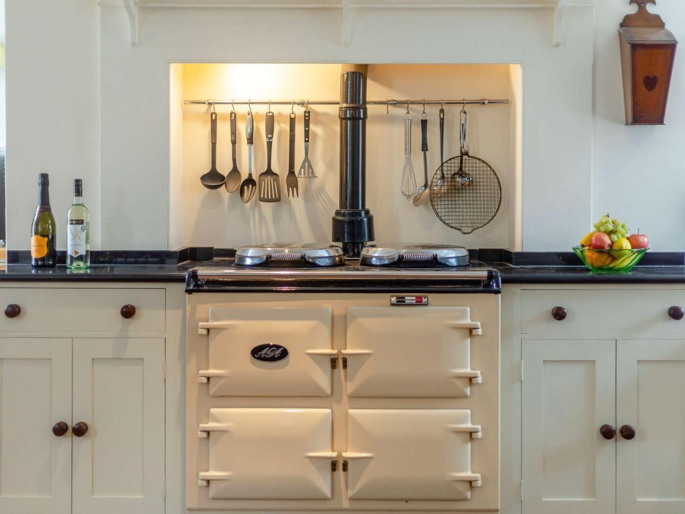 A kitchen with a built-in stove, hanging utensils, and a fruit bowl on the counter.