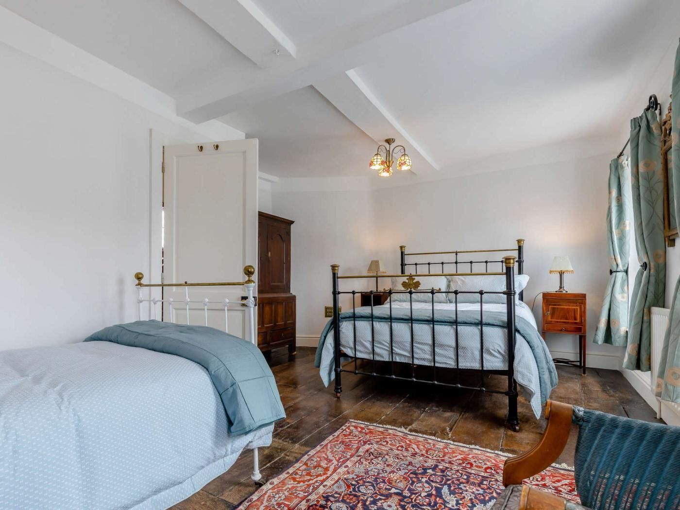A bedroom with two beds, a chandelier, a wooden cabinet, and a patterned rug.