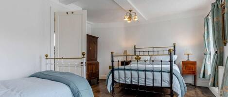 A bedroom with two beds, a chandelier, a wooden cabinet, and a patterned rug.