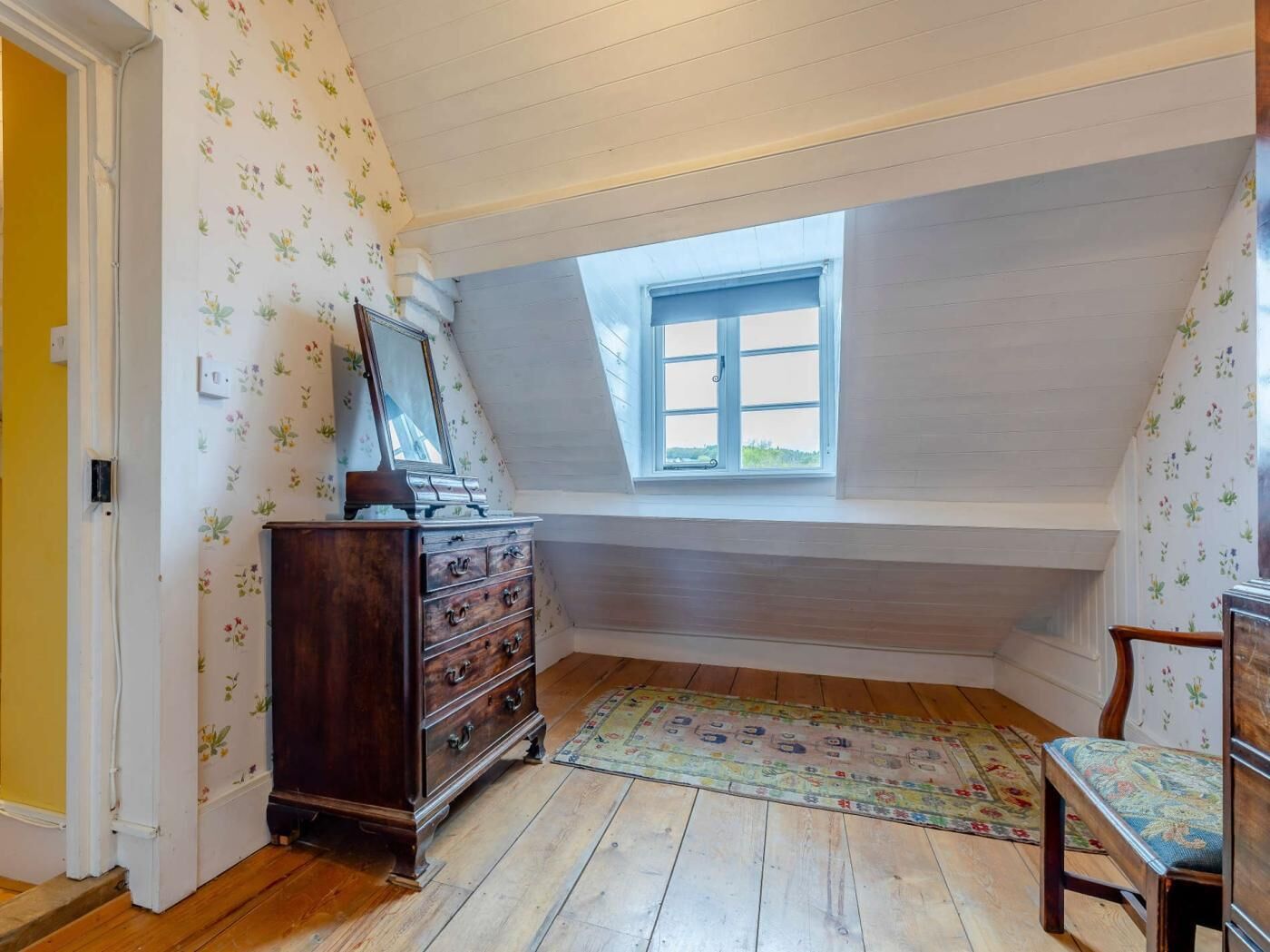 A room with a wooden dresser, a small window, a chair, and a patterned rug.