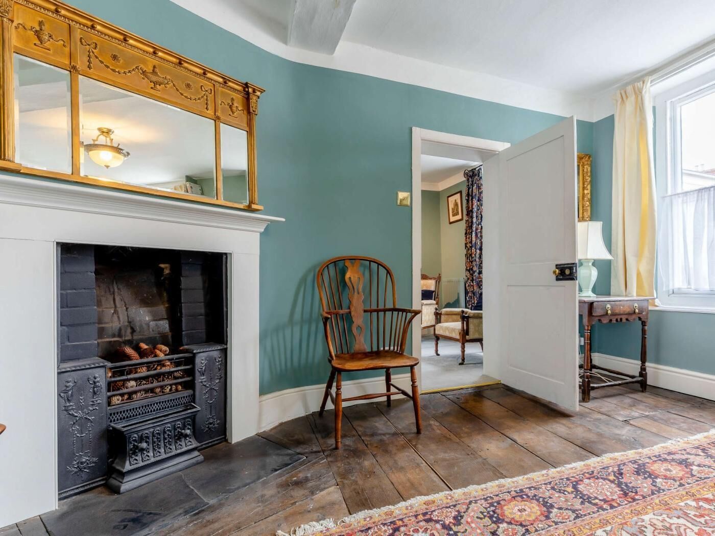 A room with a fireplace, a wooden chair, a patterned rug, and a door leading to another room.