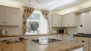 Une cuisine avec des meubles blancs, un plan de travail en bois, un four à micro-ondes et une bouilloire.