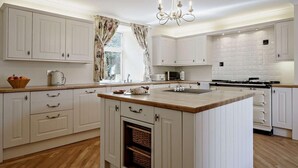 Une cuisine moderne avec des meubles blancs, un îlot central, un four encastré et un lustre.