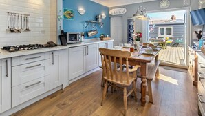 A modern kitchen with white cabinets, a wooden dining table, and a view of the beach. - 4 Bed in Newquay (oc-82951) (Newquay)