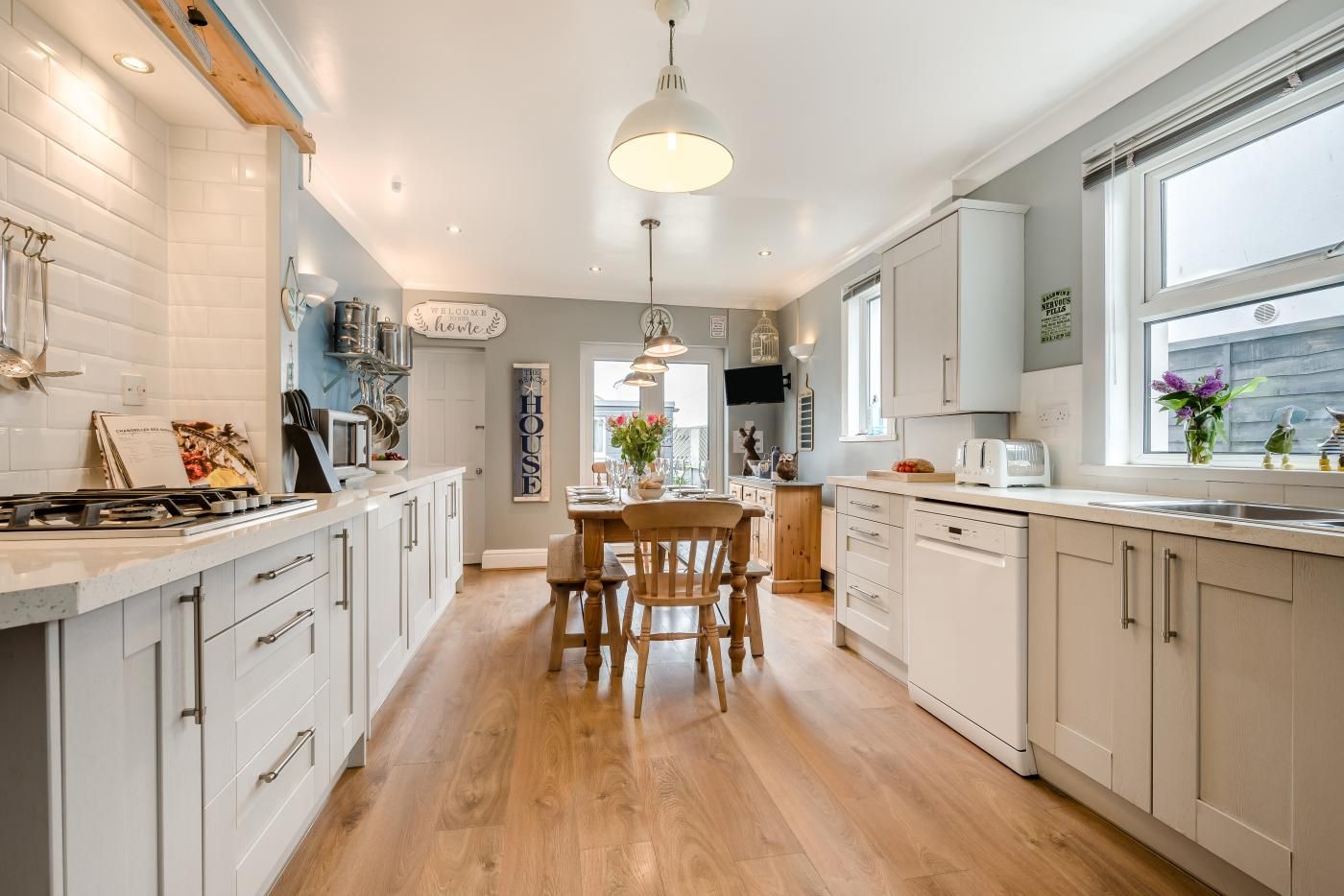 A modern kitchen with white cabinetry, a wooden dining table, and a large window providing natural light.