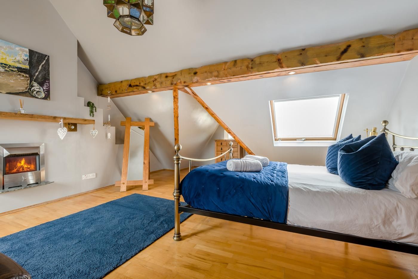 A bedroom with a sloped ceiling, a fireplace, a bed with blue bedding, and a window.