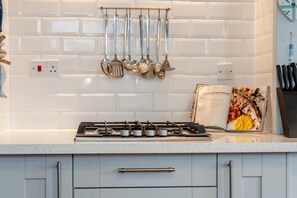 A kitchen with a gas stove, hanging utensils, and a cookbook on the counter. - 4 Bed in Newquay (oc-82951) (Newquay)