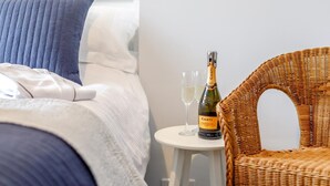 Ett hotellrum med en säng, en flätad fåtölj, ett litet bord med en flaska Canti Prosecco och två glas.
