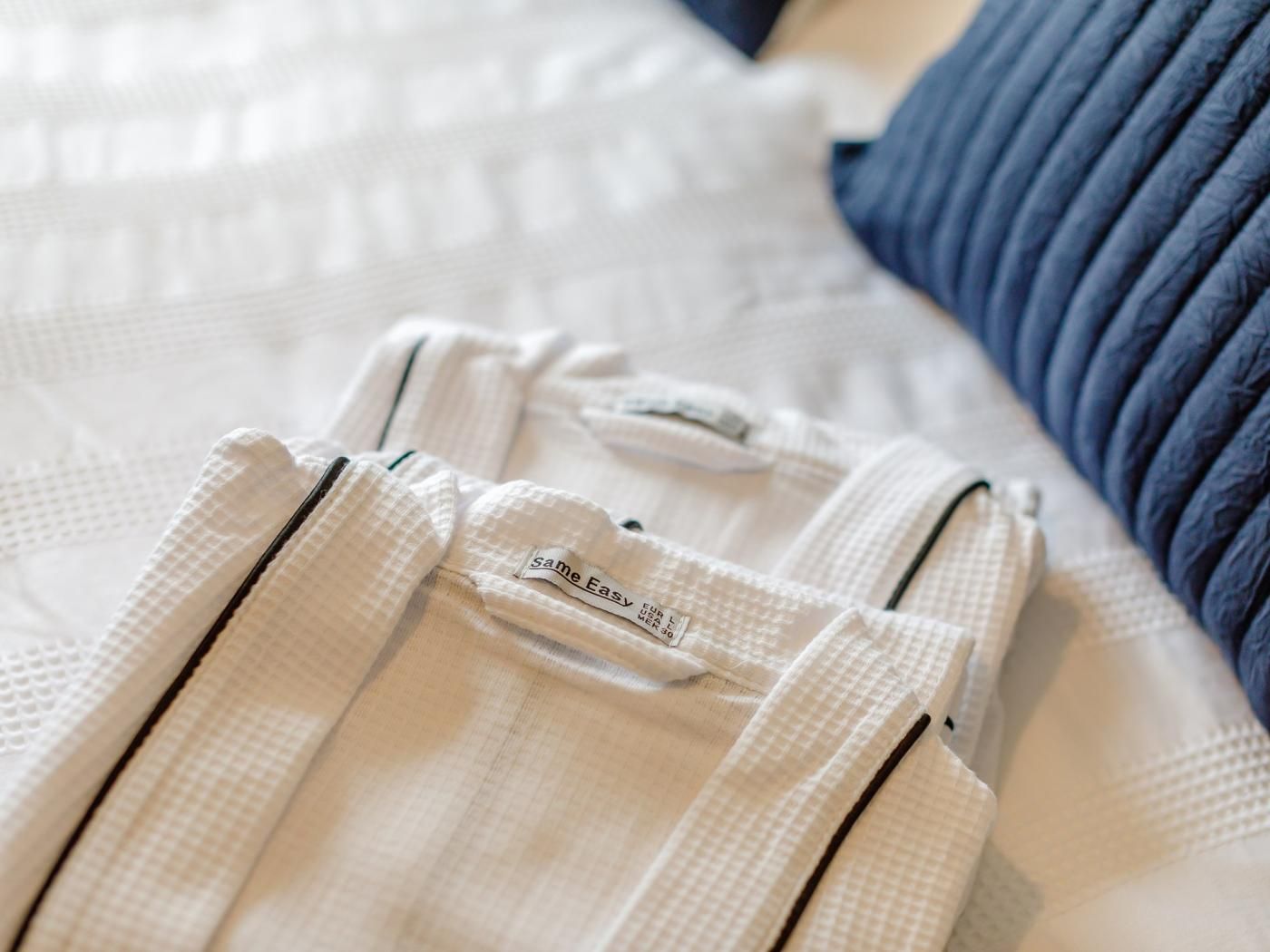 A bed with a white quilt and a blue pillow.