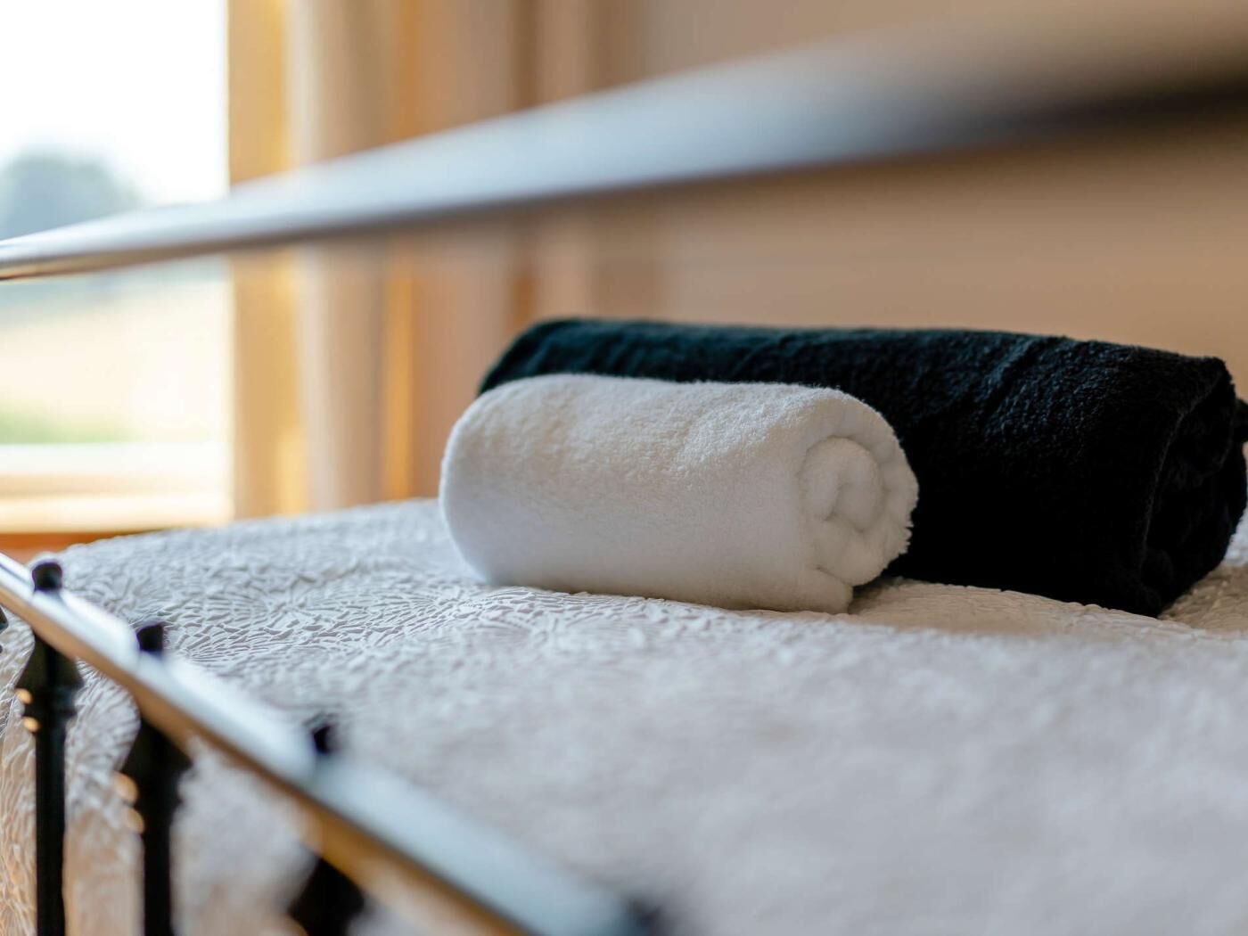 A neatly folded white towel and a black towel on a textured white bedspread.