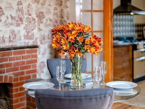 A dining table set with plates and glasses, a vase with flowers, and a brick wall with a mural in the background. - 2 Bed in Ventnor (oc-82973) (Wroxall)