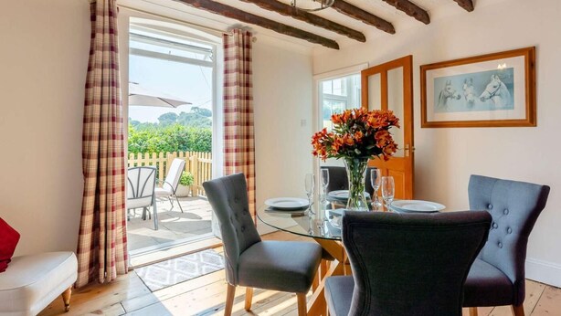 Un coin repas avec une table en verre, deux chaises, un vase de fleurs et une vue sur une terrasse extérieure, accessible par une porte vitrée.