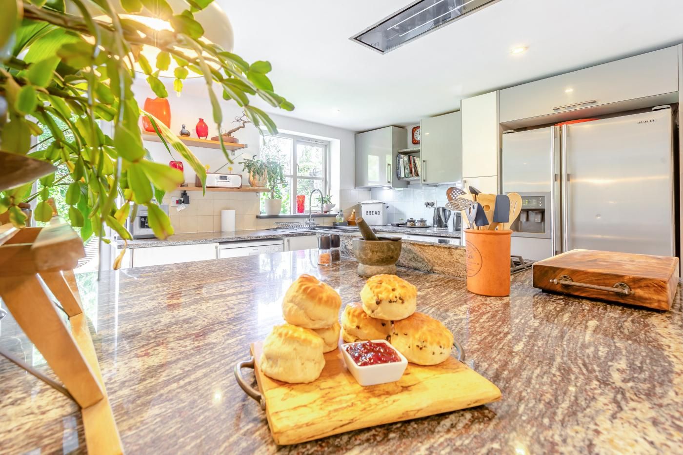 Une cuisine moderne avec un plan de travail en marbre, une planche à découper en bois sur laquelle sont disposées des pâtisseries, et un réfrigérateur en acier inoxydable.
