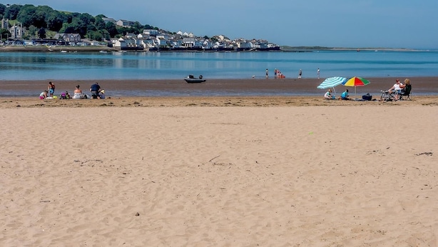 Una playa con gente, un bote y casas al fondo.