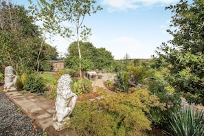 Ein angelegter Garten mit Steinskulpturen, einer Terrassenfläche und verschiedenen Pflanzen.