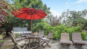 Un patio exterior con una mesa redonda, cuatro sillas, un paraguas rojo y un jacuzzi.