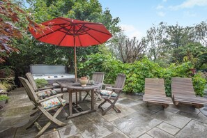 Eine Terrasse im Freien mit einem runden Tisch, vier Stühlen, einem roten Sonnenschirm und einem Whirlpool.