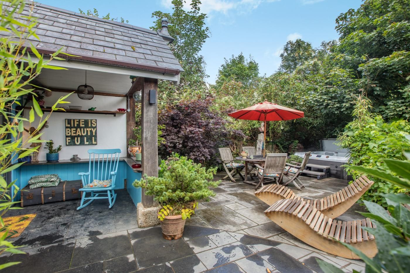 A patio area with a table and chairs, a red umbrella, and a sign that reads 'LIFE IS BEAUTY FULL.'