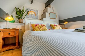 Ein ordentlich bezogenes Bett mit Streifenmuster, eine Nachttischlampe und ein wandmontierter Spiegel.