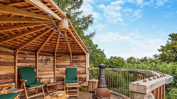 A wooden cabin with a deck, two green chairs, a table with a pot, and a chimney. - 2 Bed in Craven Arms (oc-83166) (Clun)