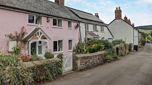 A pink building with a white door, a stone wall, and a garden with flowers. - 2 Bed in Craven Arms (oc-83166) (Clun)