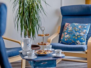 A room with a blue armchair, a small table with a teapot, cups, and a tiered tray of pastries. - 2 Bed in Craven Arms (oc-83166) (Clun)